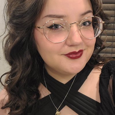 A close-up image of Nonnie, a young white woman with dark curled hair and round gold glasses. She is wearing red lipstick and smirking slightly.