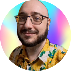 Treyson, a Caucasian nonbinary person in their late 30s. Their head is shaved, and they have a mustache and beard. They are wearing black glasses, a yellow eyebrow piercing, and a sunflower-print button-down shirt.