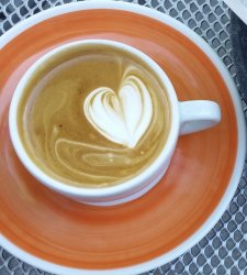 A latte with a heart made of milk foam in a mug on an orange ceramic plate.