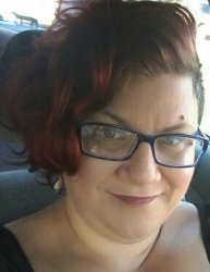 White woman in mid 40s with red curly hair and blue glasses
